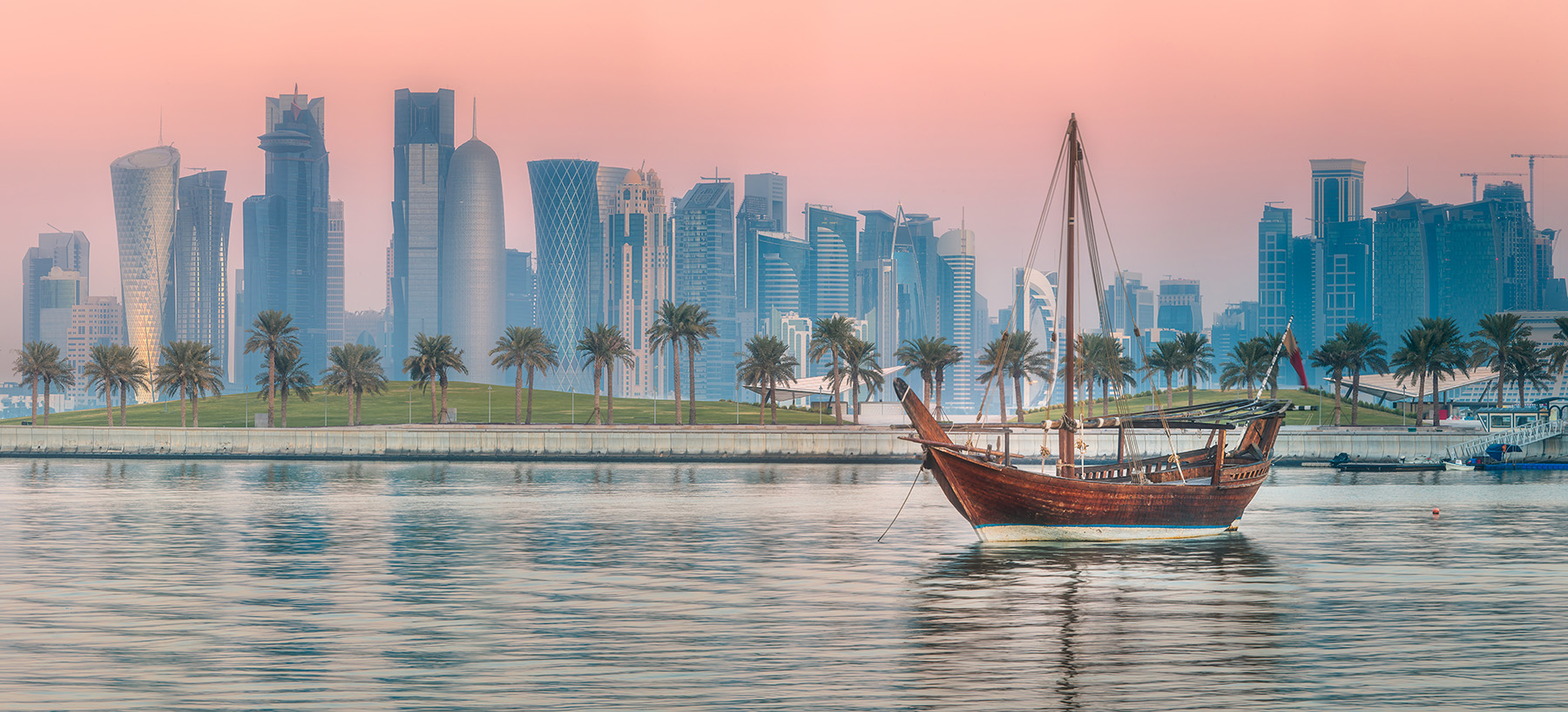 The photograph shows a dhow, an Arabian boat that inspired the design of the Al Janoub stadium, sailing on water with an urban skyline in the background. 