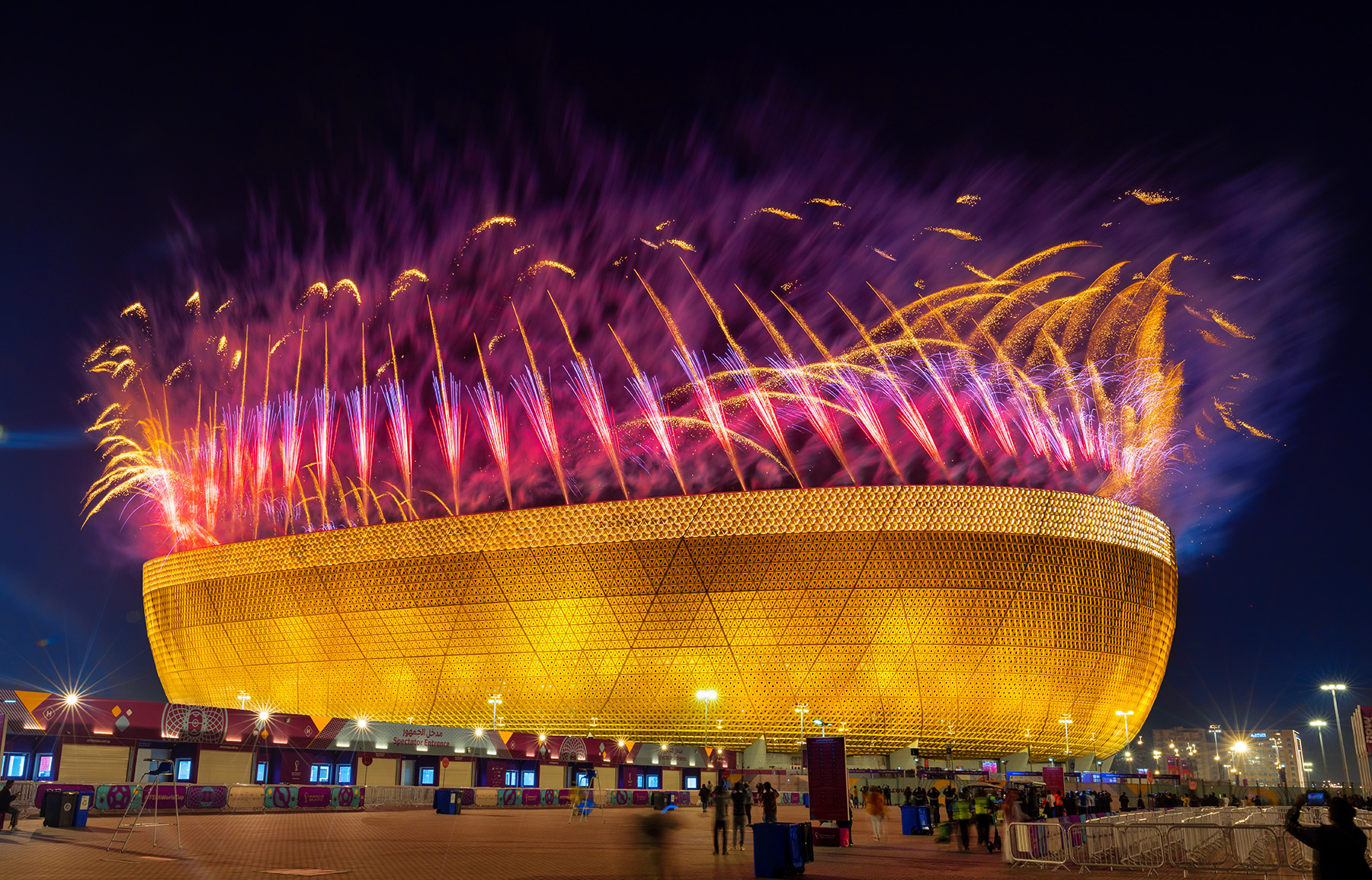 The photograph shows fireworks exploding in the air above the Lusail Stadium at night. 