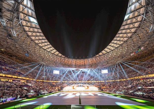 The photograph shows a soccer stadium filled with people and spotlights.