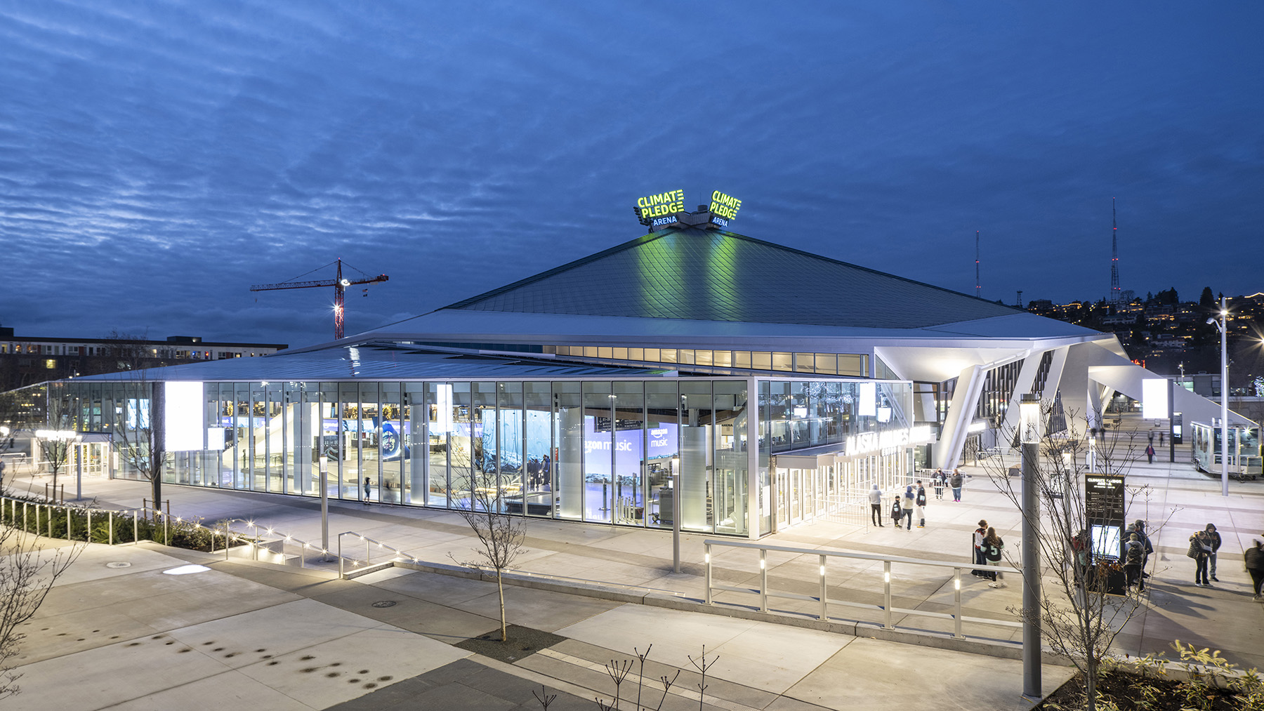 A building with a glass facade has a pointy roof. People walk around outside the building. 