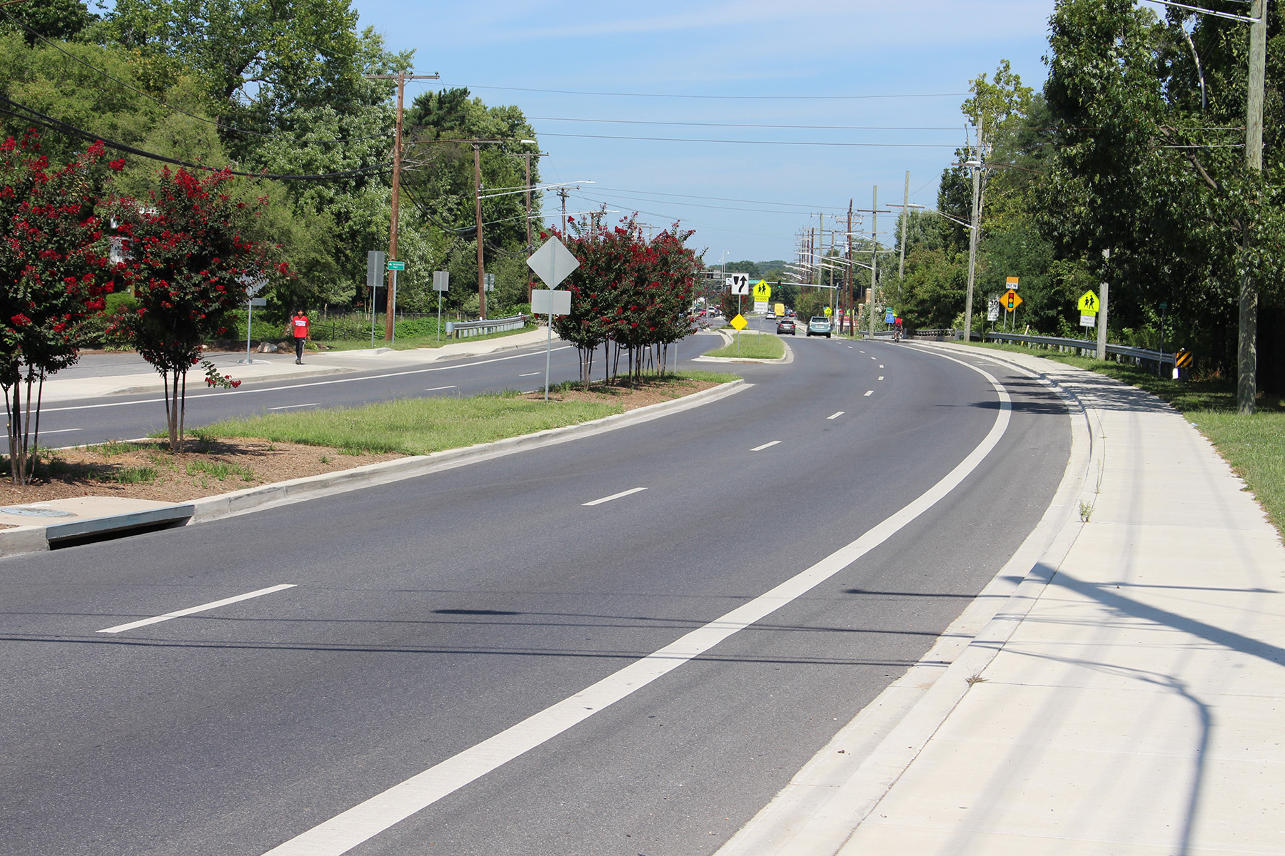 Image shows a road with street lines. There is a tree-lined median and tress in the distance. 