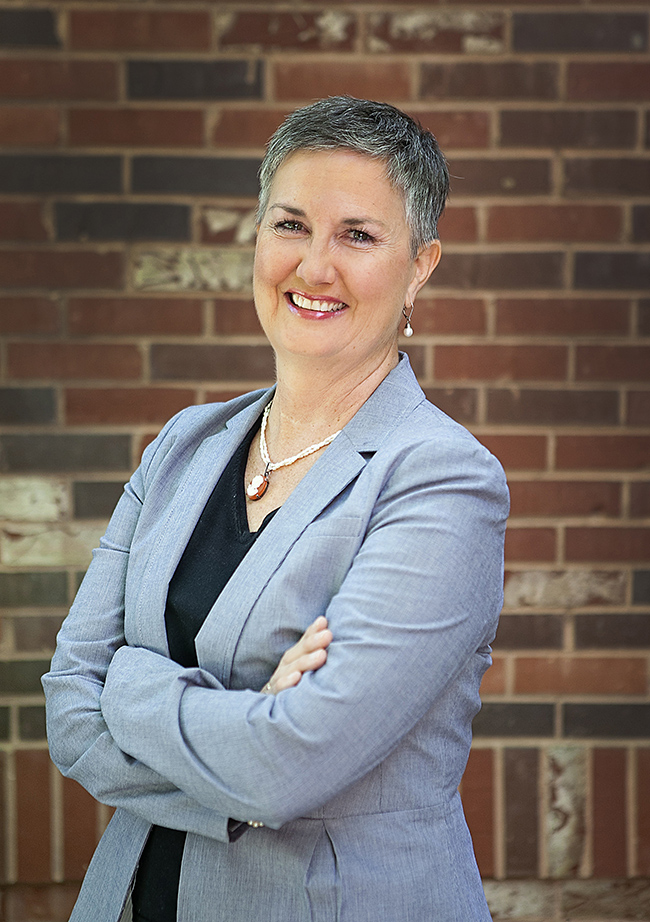 Woman wearing gray blazer with short hair smiles at the camera.