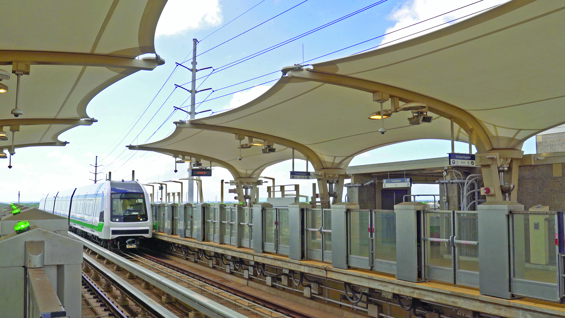A train pulls into the Keoneae/UH-West Oahu station. The large tensile fabric canopies at the first stations proved expensive and difficult to construct. (Image courtesy of HART) 