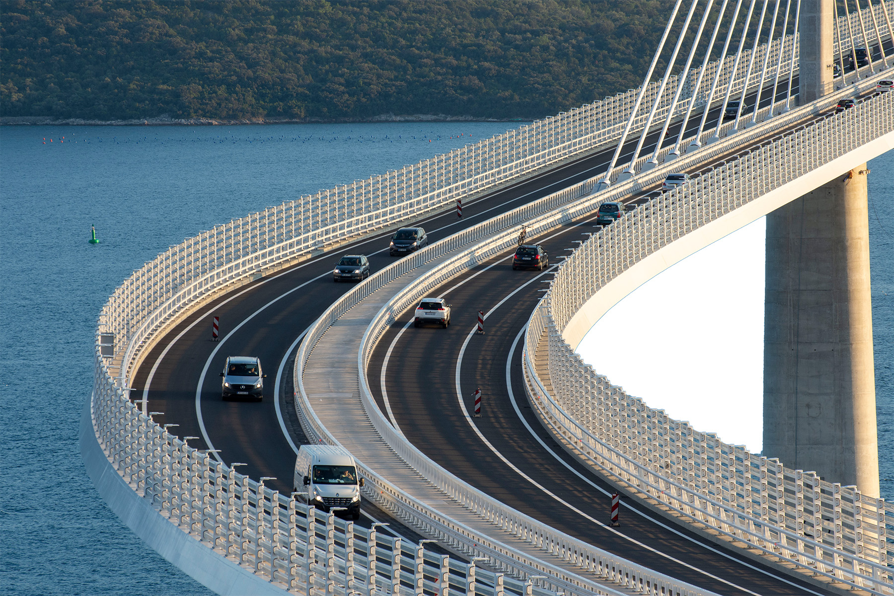 Cars cross the bridge, traveling on a curved section close to the channel shore. 