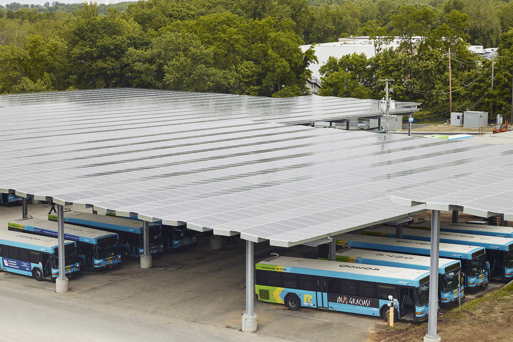 The photograph shows electric buses beneath a canopy covered in solar panels. 