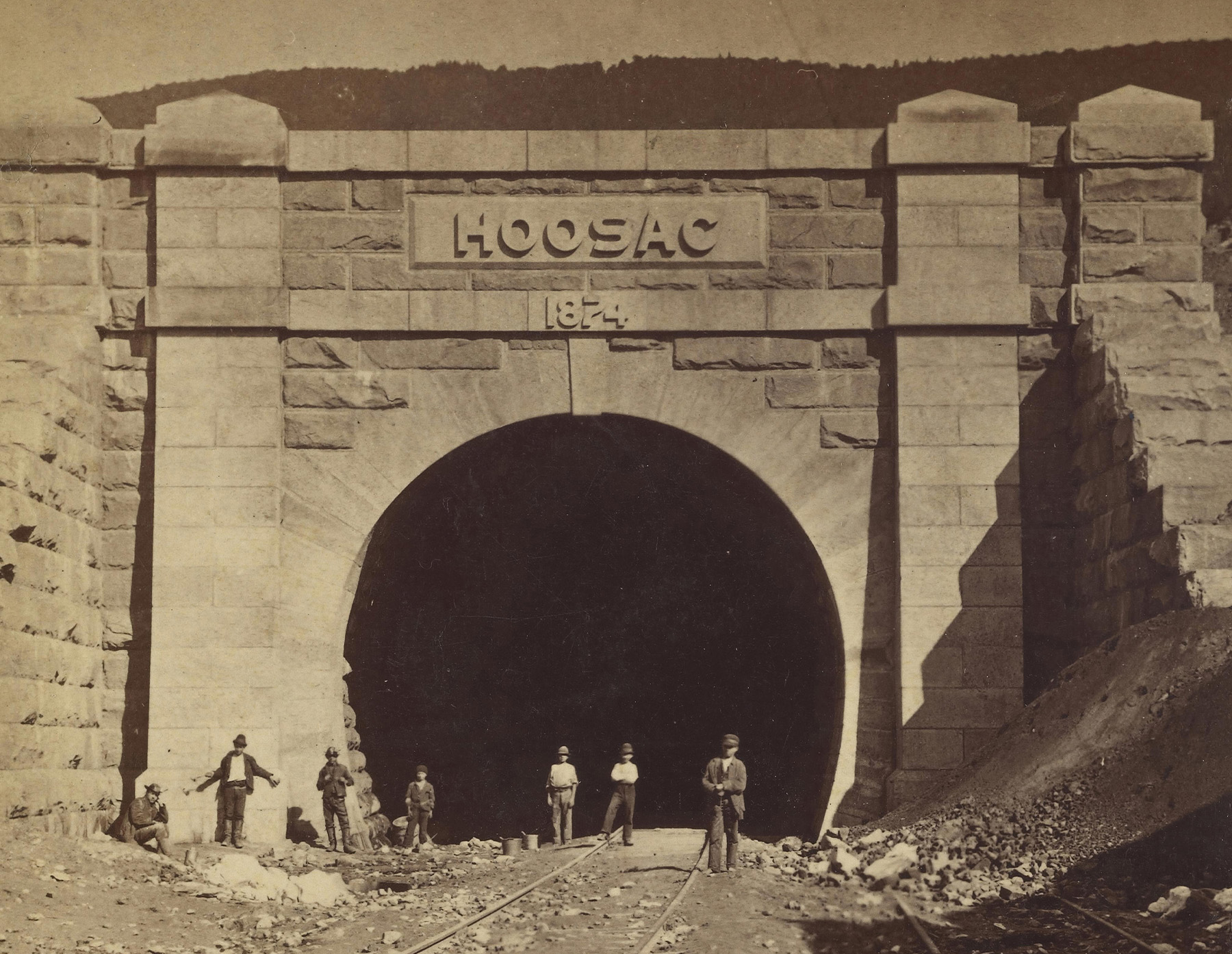 Men stand outside a railroad tunnel. 