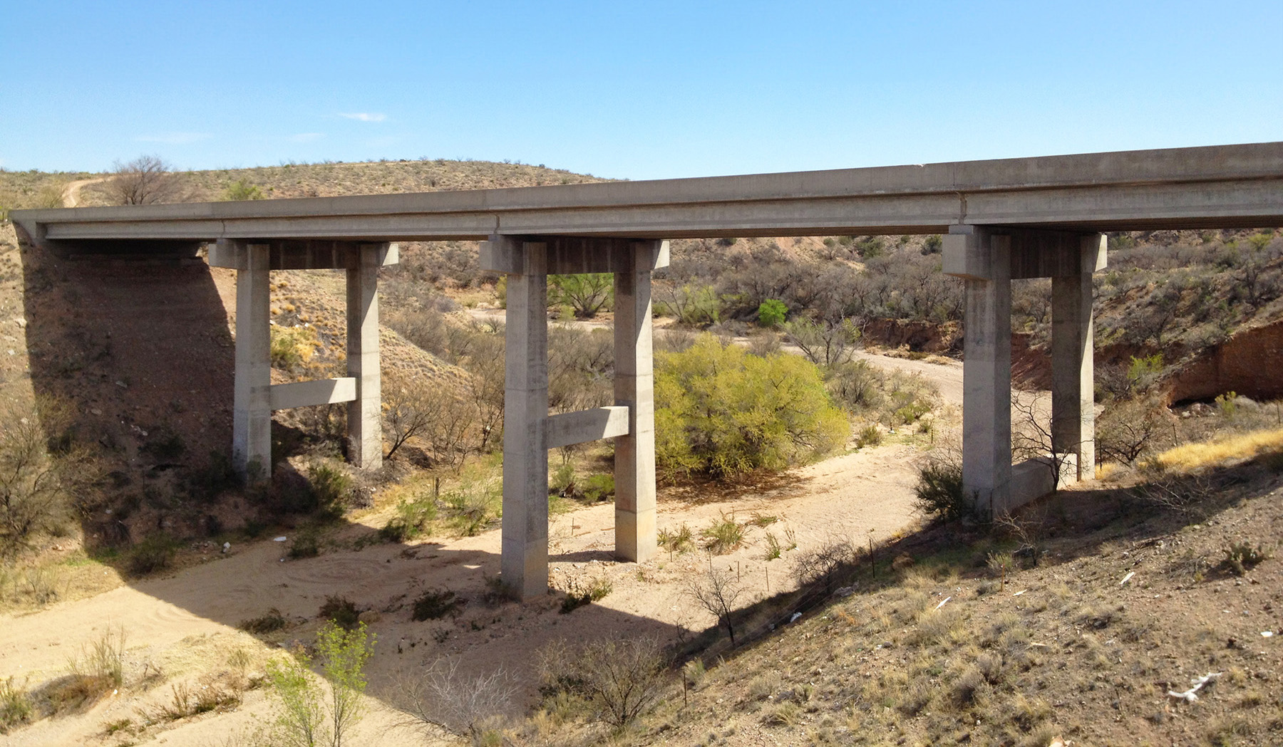 Image shows a bridge over a dry streambed. 
