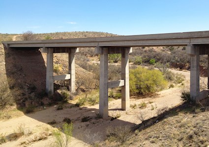 Image shows a bridge over a dry streambed. 