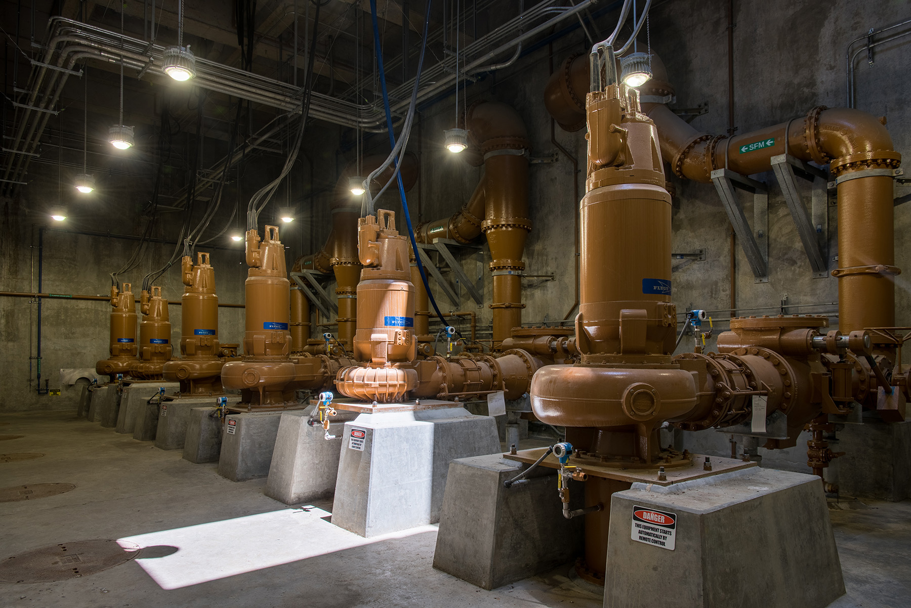 Large, oblong orange tanks are attached to concrete platforms. The tanks have arrays of pipes connected to the ceiling.