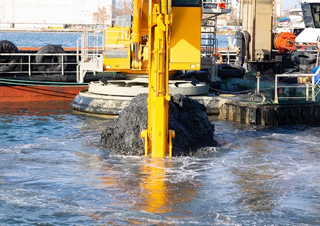 Sediment is being dredged from a body of water by large equipment. 