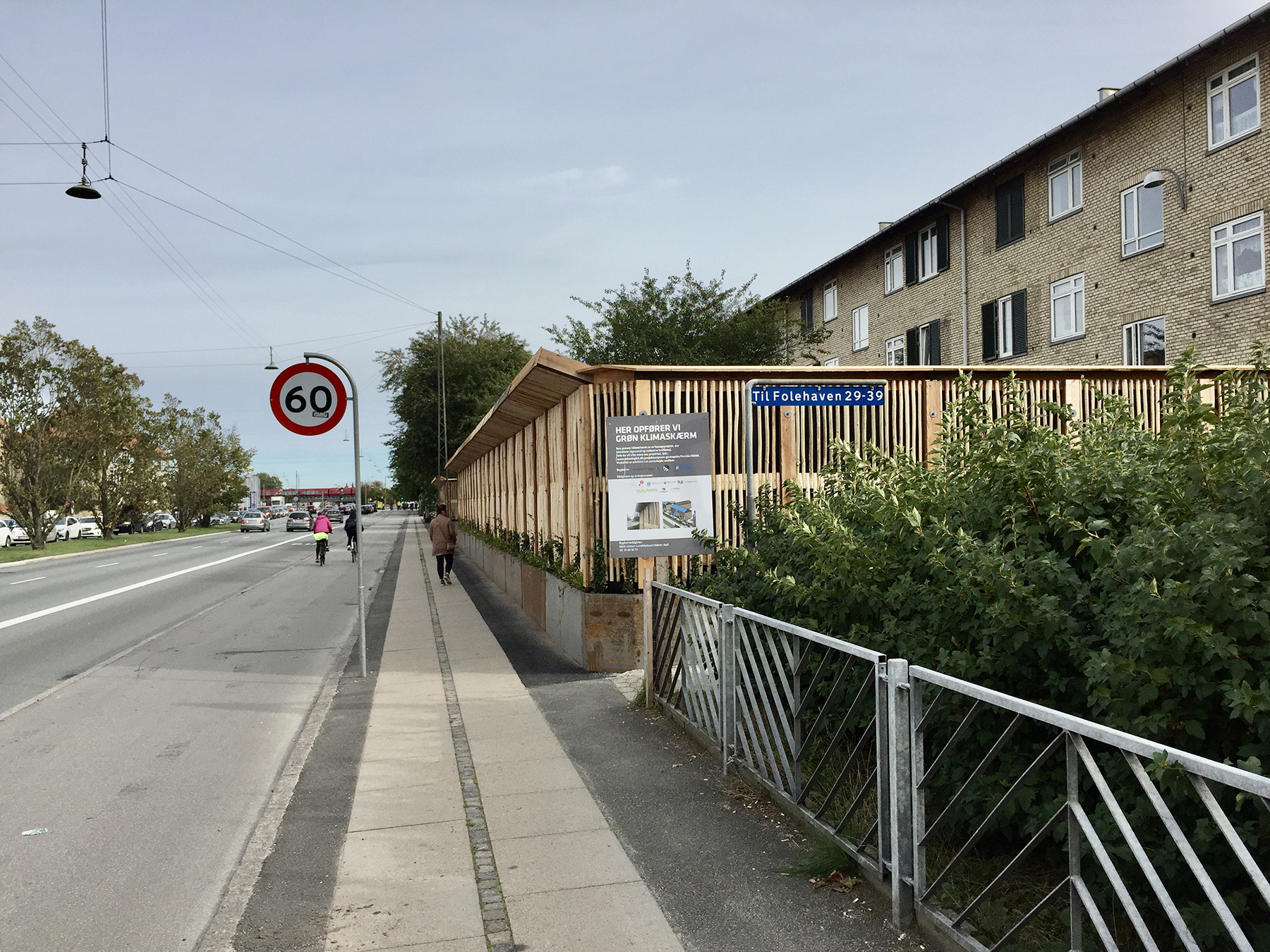 a barrier with vegetation sits between a street and an apartment building