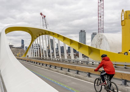 a cyclist crosses a bridge with the city skyline in the background