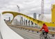 a cyclist crosses a bridge with the city skyline in the background