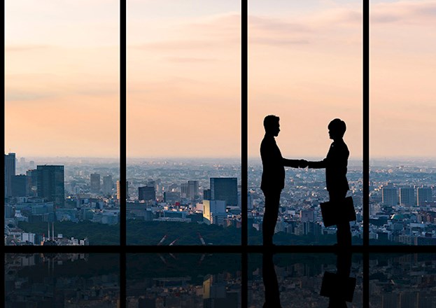 A city skyline is highlighted against the sunset. Two executives are shown shaking hands in silhouette.