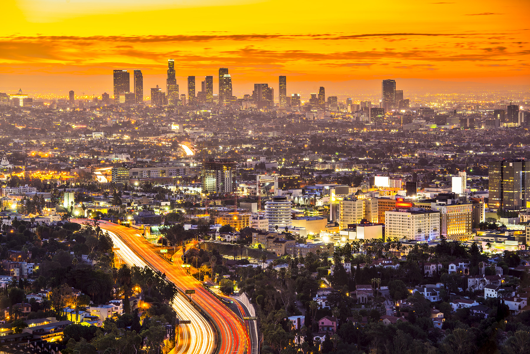 A sprawling horizon of buildings, skyscrapers, and roads with an orange sky in the background.