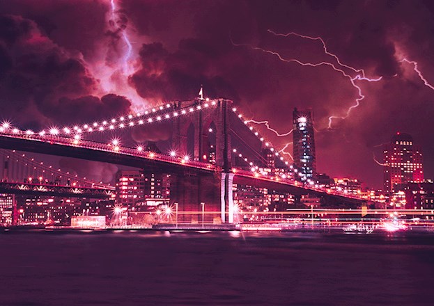 The photograph depicts a large suspension bridge, illuminated at night against an urban skyline, during a lightning storm.