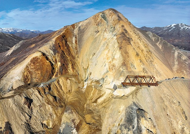 Photograph shows a steel truss bridge under construction on a mountainside.