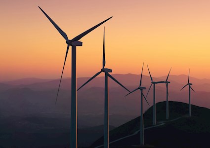 Six 3-blade while windmills are lined up on a mountainous parcel of land.