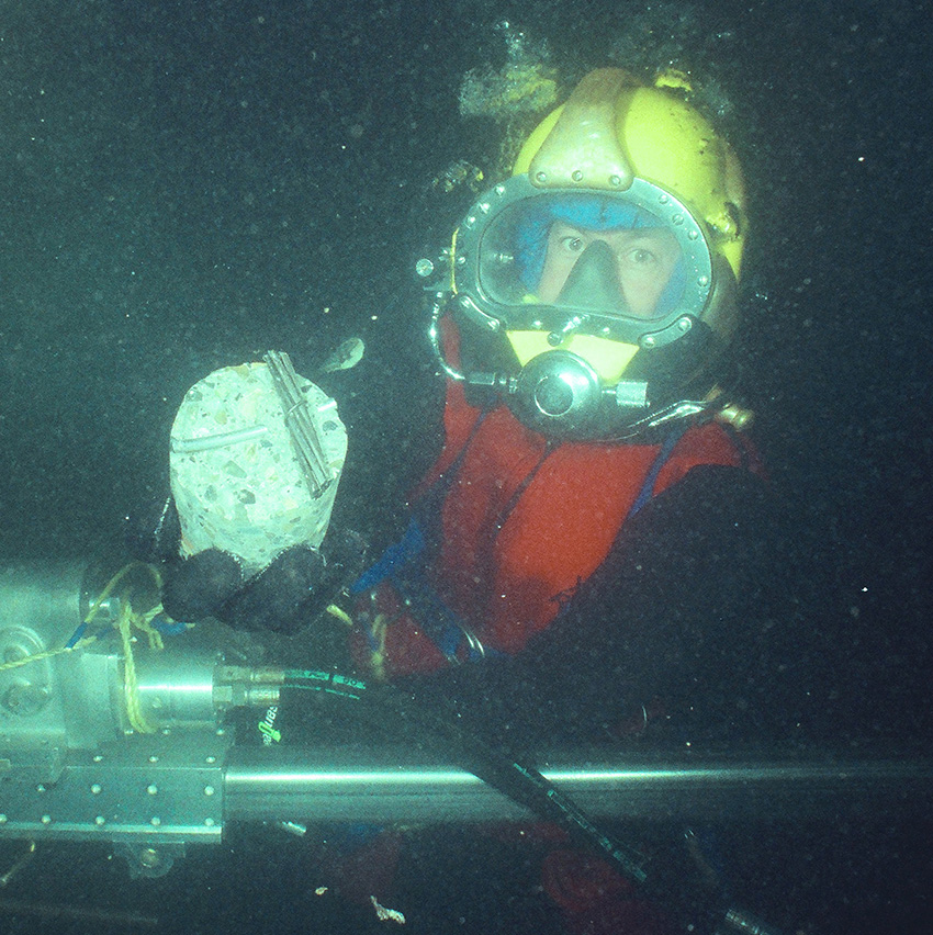 A man holds a piece of equipment that he’s using to inspect a corroded mooring.