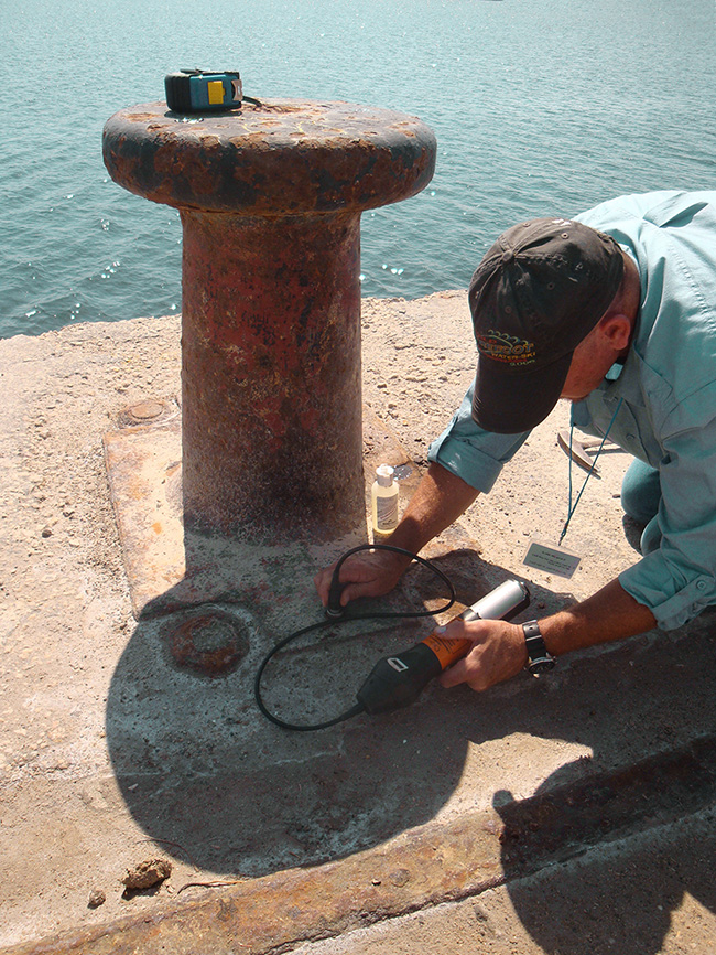 A man holds a piece of equipment that he’s using to inspect a corroded mooring.