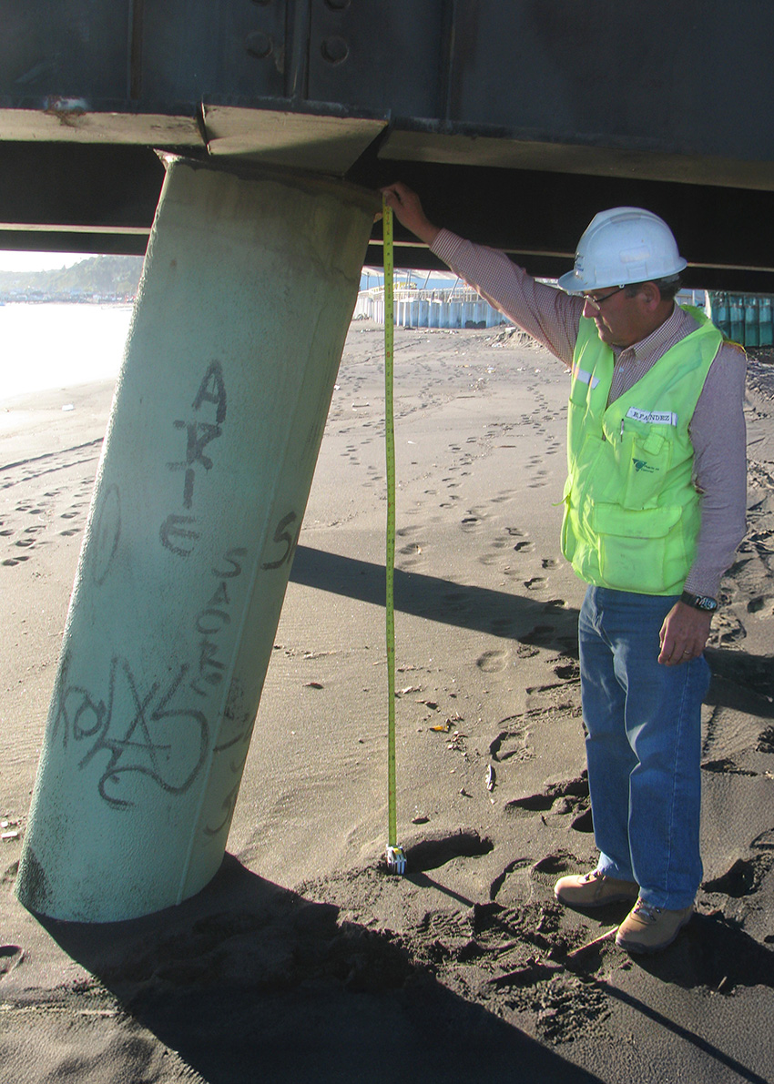 A man measures a displaced pile. The pile has moved a foot from its original location.