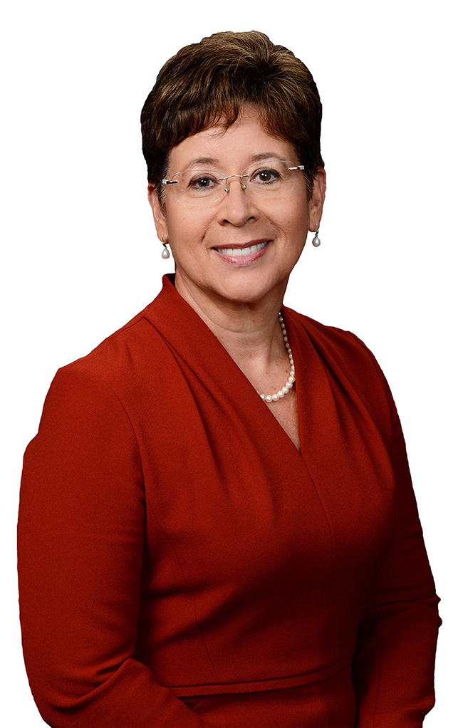 A woman with short, dark hair and glasses smiles at the camera.