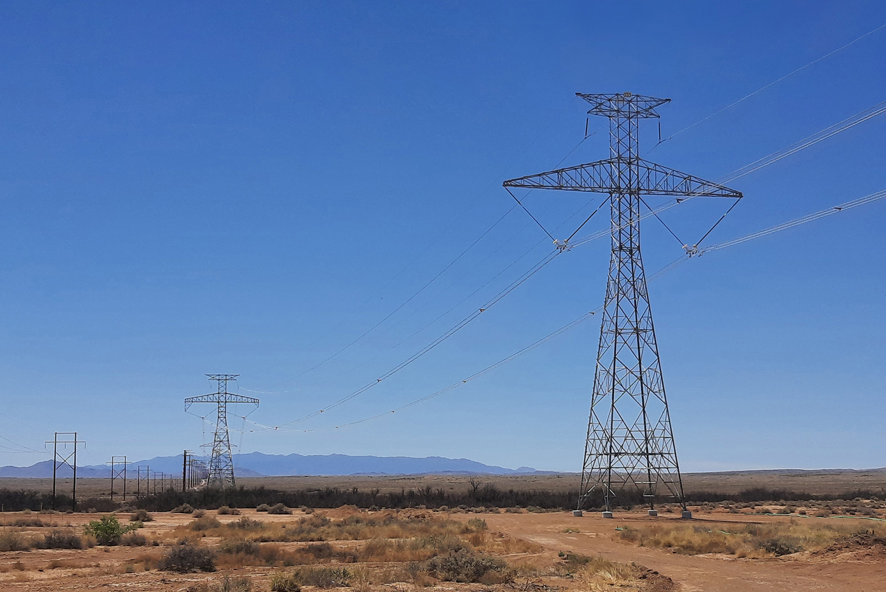 Photo shows a long row of power line transmission structures set in a desert landscape. 