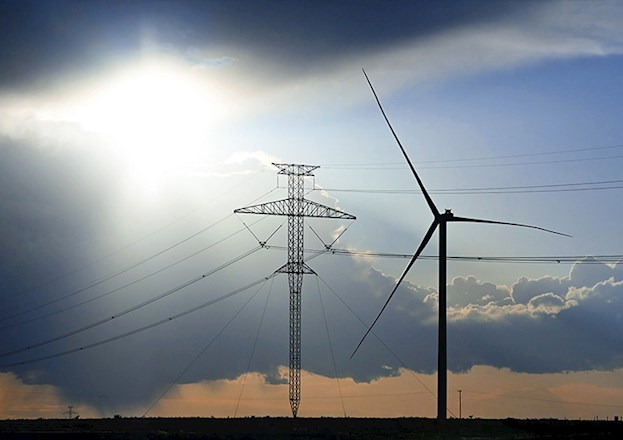 A power line structure and a wind mill are set in a desolate, night-time landscape.