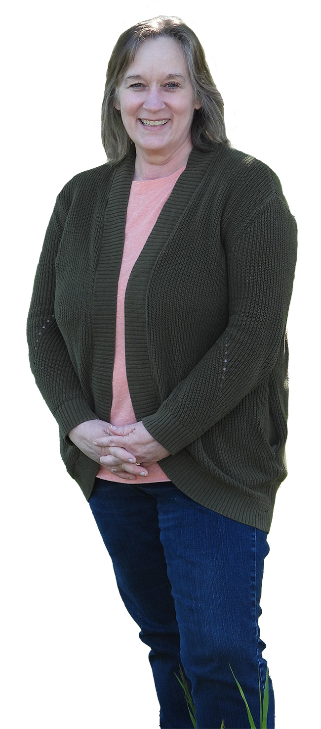 A woman with shoulder-length hair, wearing a pink shirt and a cardigan, smiles. 
