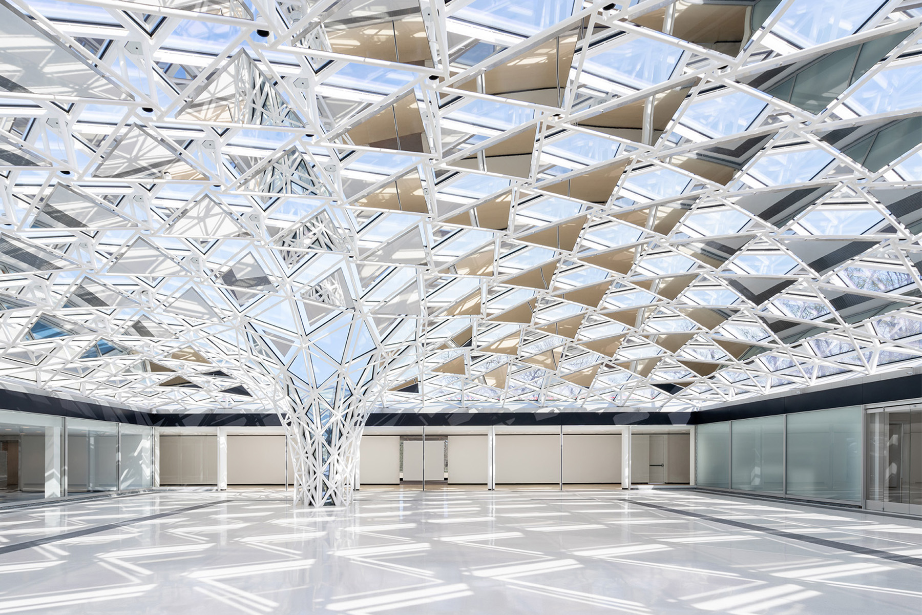 A funnel-shaped canopy made from triangulated glazed segments swoops down to make contact with the reflective surface of the floor in the newly enclosed courtyard space.