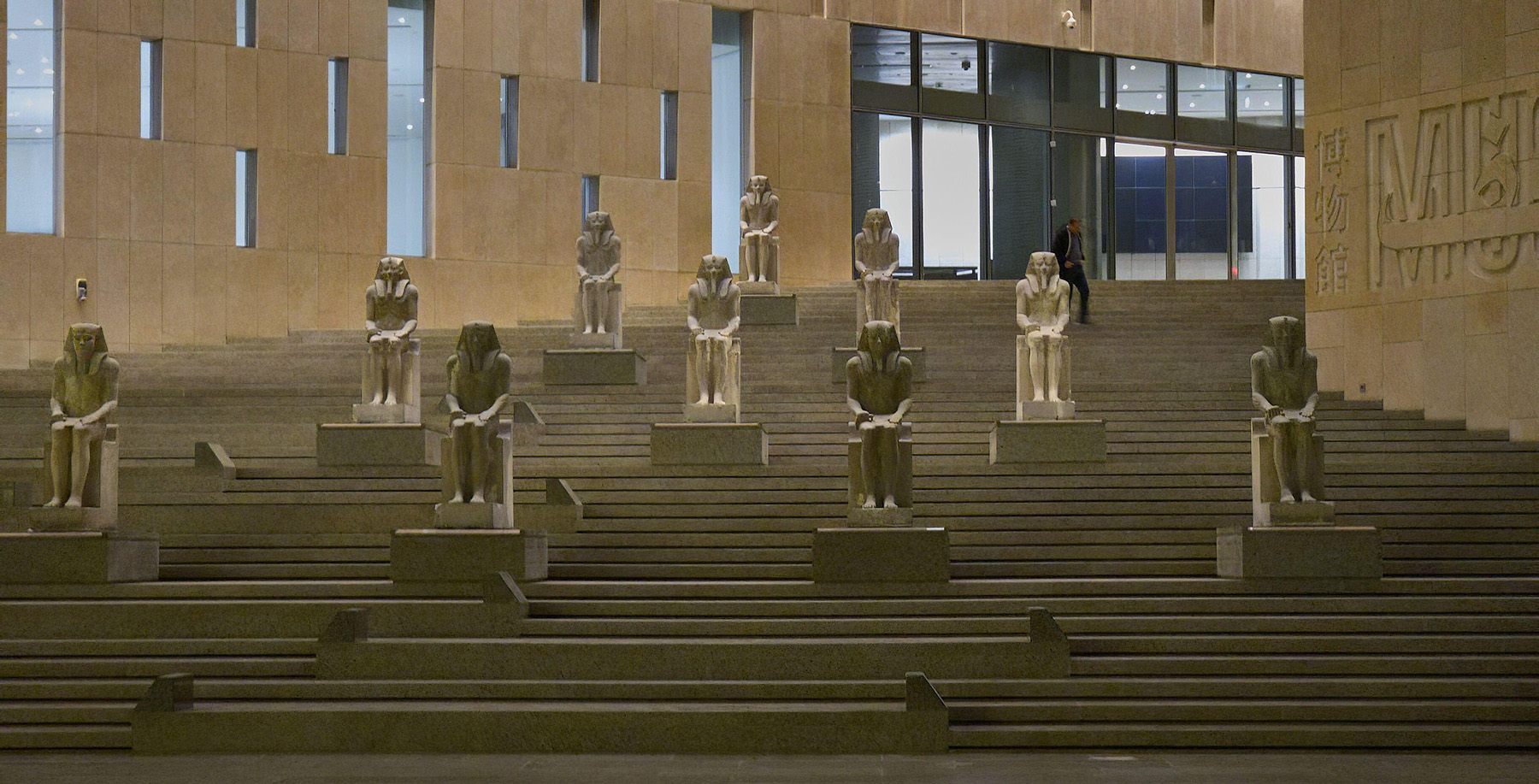 Large statues of pharaohs populate a multilevel staircase in a museum.