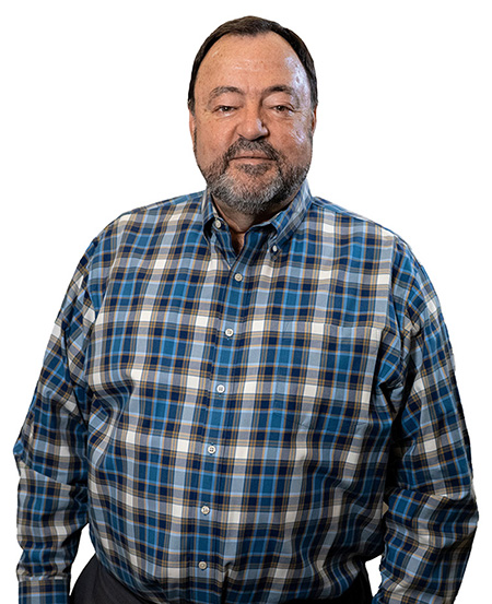 A man with a greying beard, wearing a blue plaid shirt, looks out at the camera. 