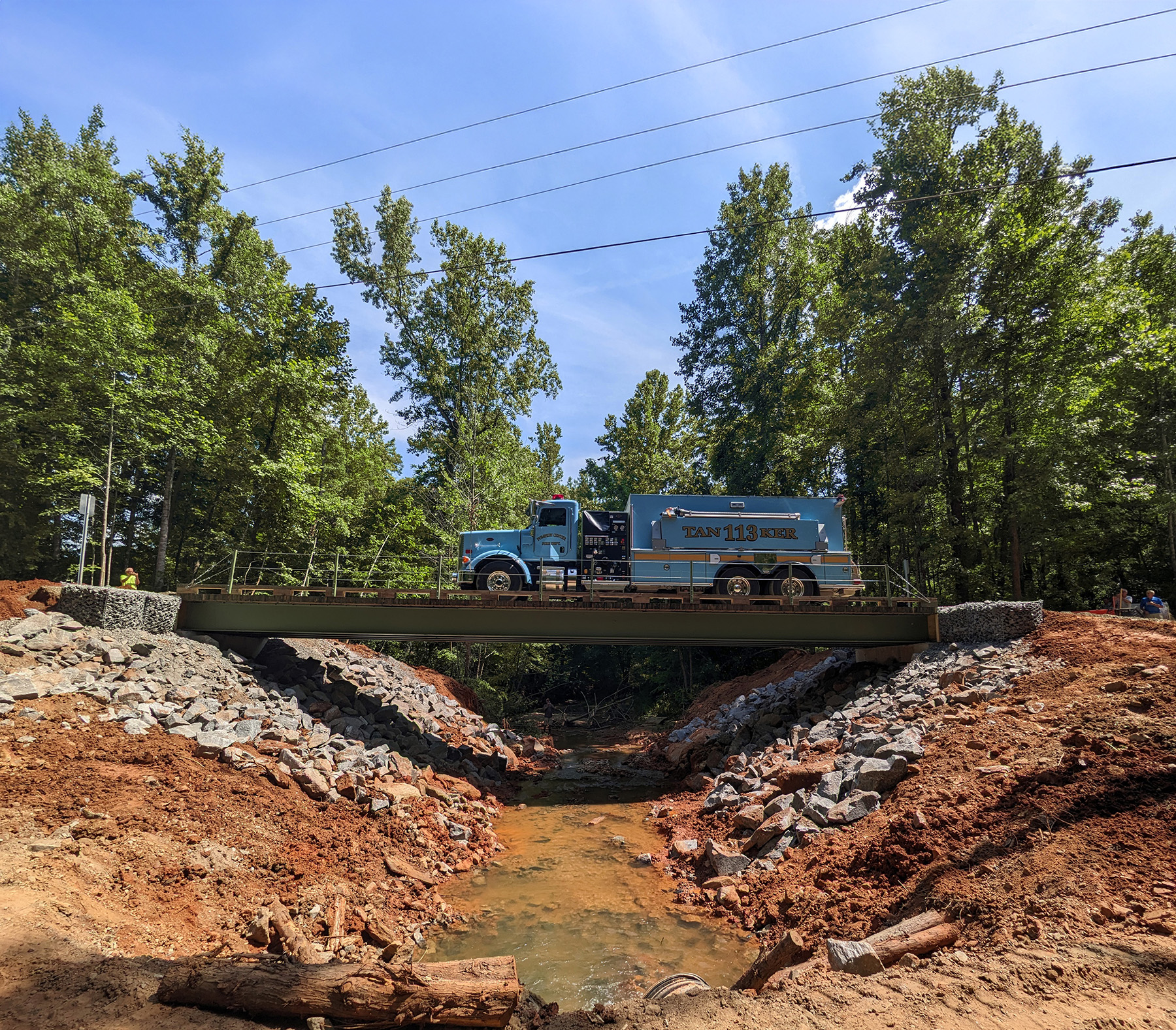 A blue commercial truck crosses a steel bridge. Below the bridge is water. 
