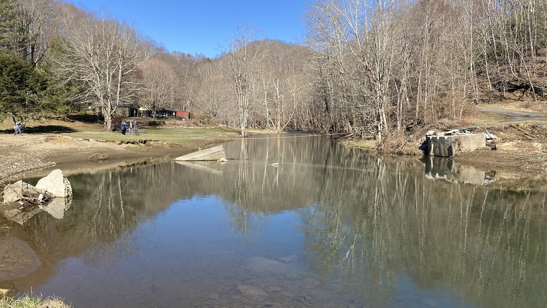 Photo shows pieces of a collapsed bridge. One piece is on the bank and the other is in the water. 