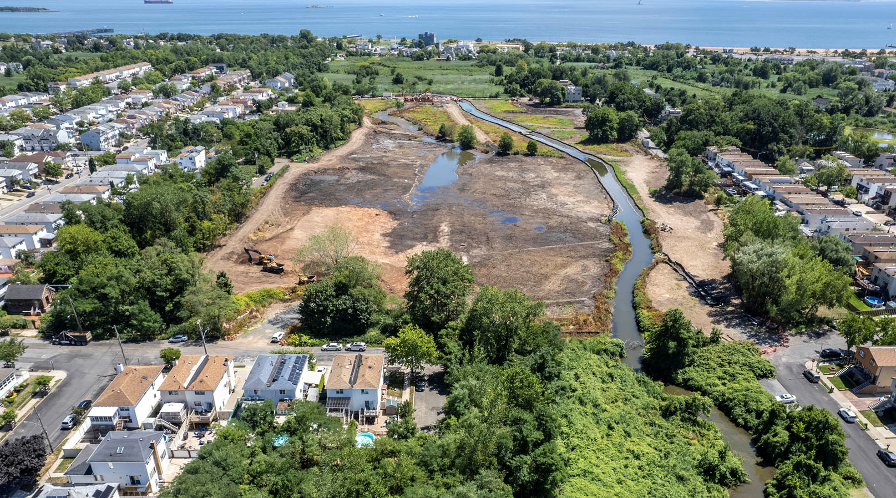 Suburban homes and trees surround a wetlands area under construction. 