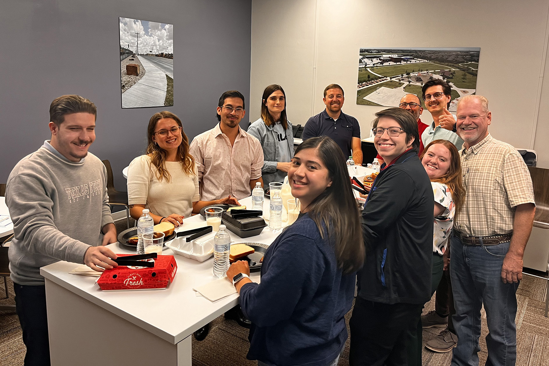 Smiling people stand around a raised white countertop that is covered in food takeout boxes.