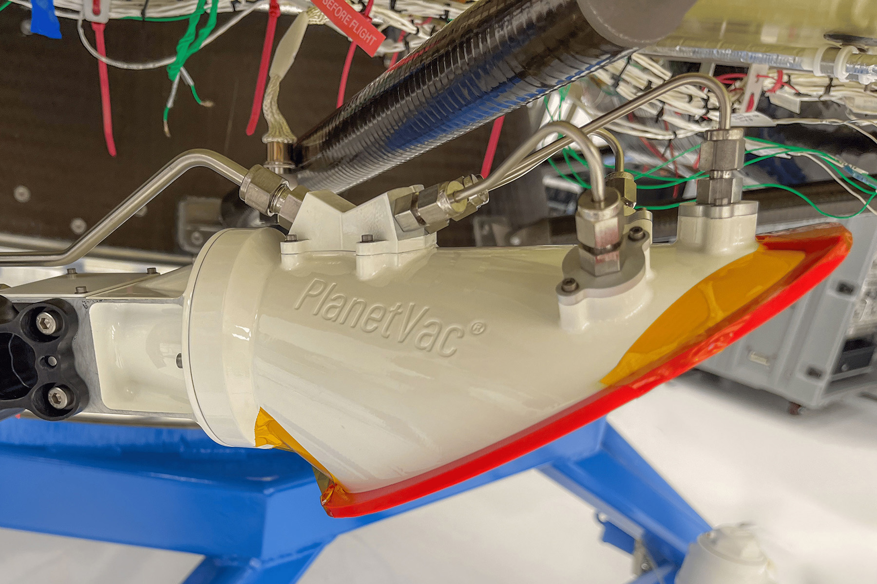 A white, red, orange, and blue cylindrical piece of equipment reads “PlanetVac.”