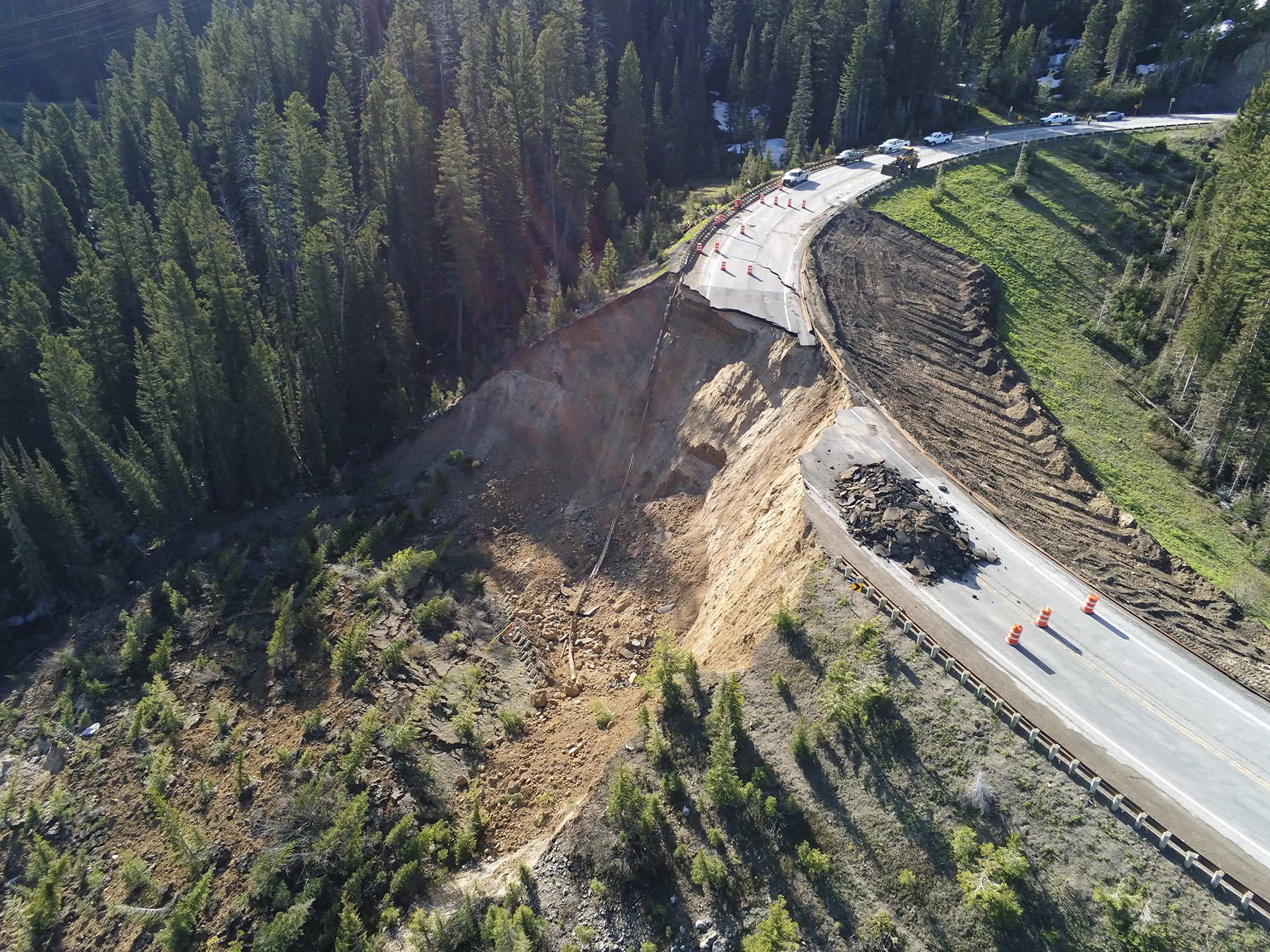 A portion of an earthen embankment under a roadway has collapsed. The road is divided in two and there is a lot of rubble on the road. 