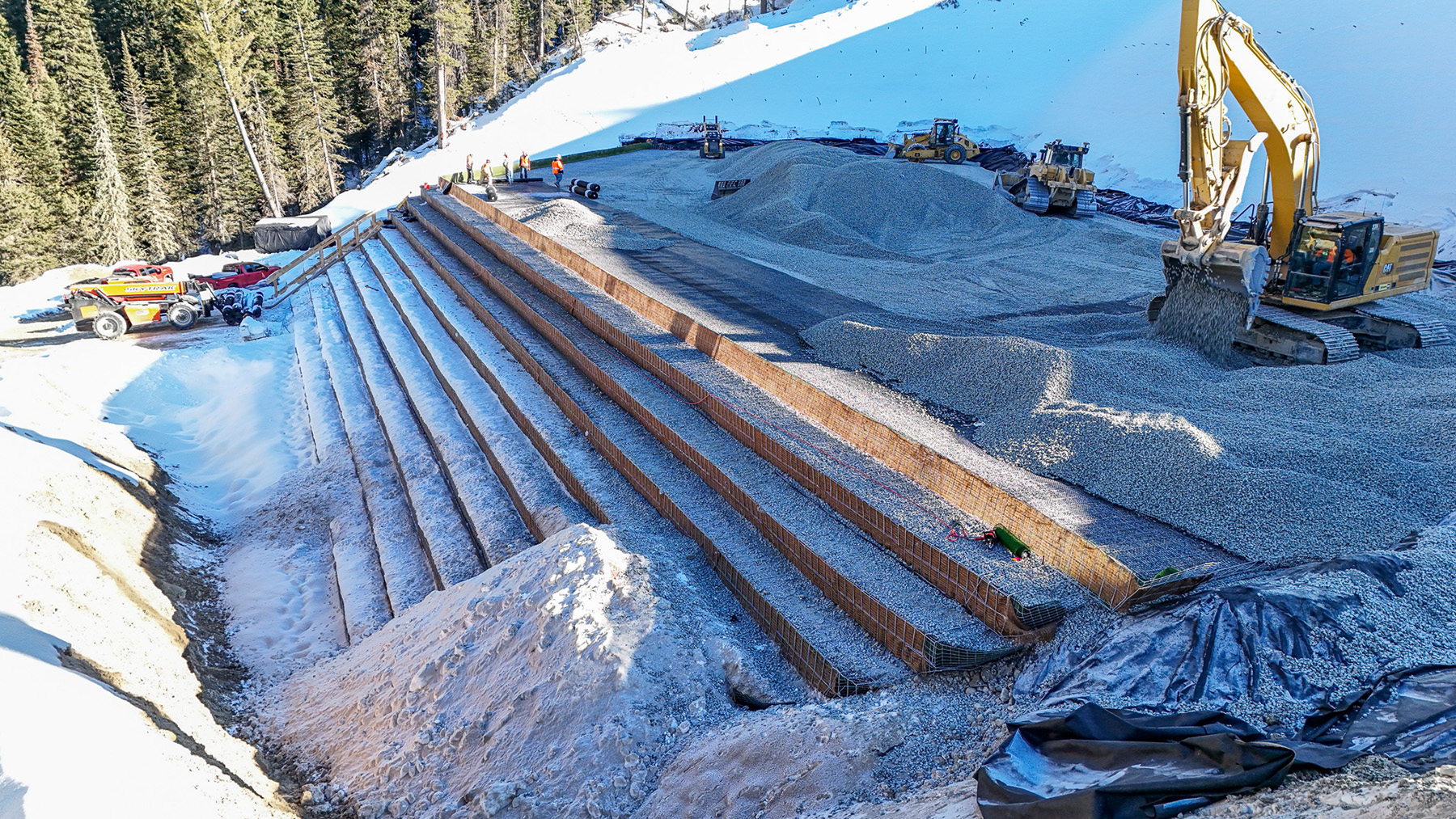 Photo shows the layers that comprise an earthen embankment. The structure is stepped and there’s snow covering the ground and the structure. 