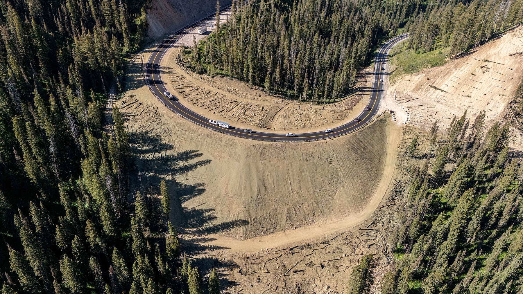 Aerial view of the completed construction of an earthen embankment. Trucks can be seen on the roadway. 