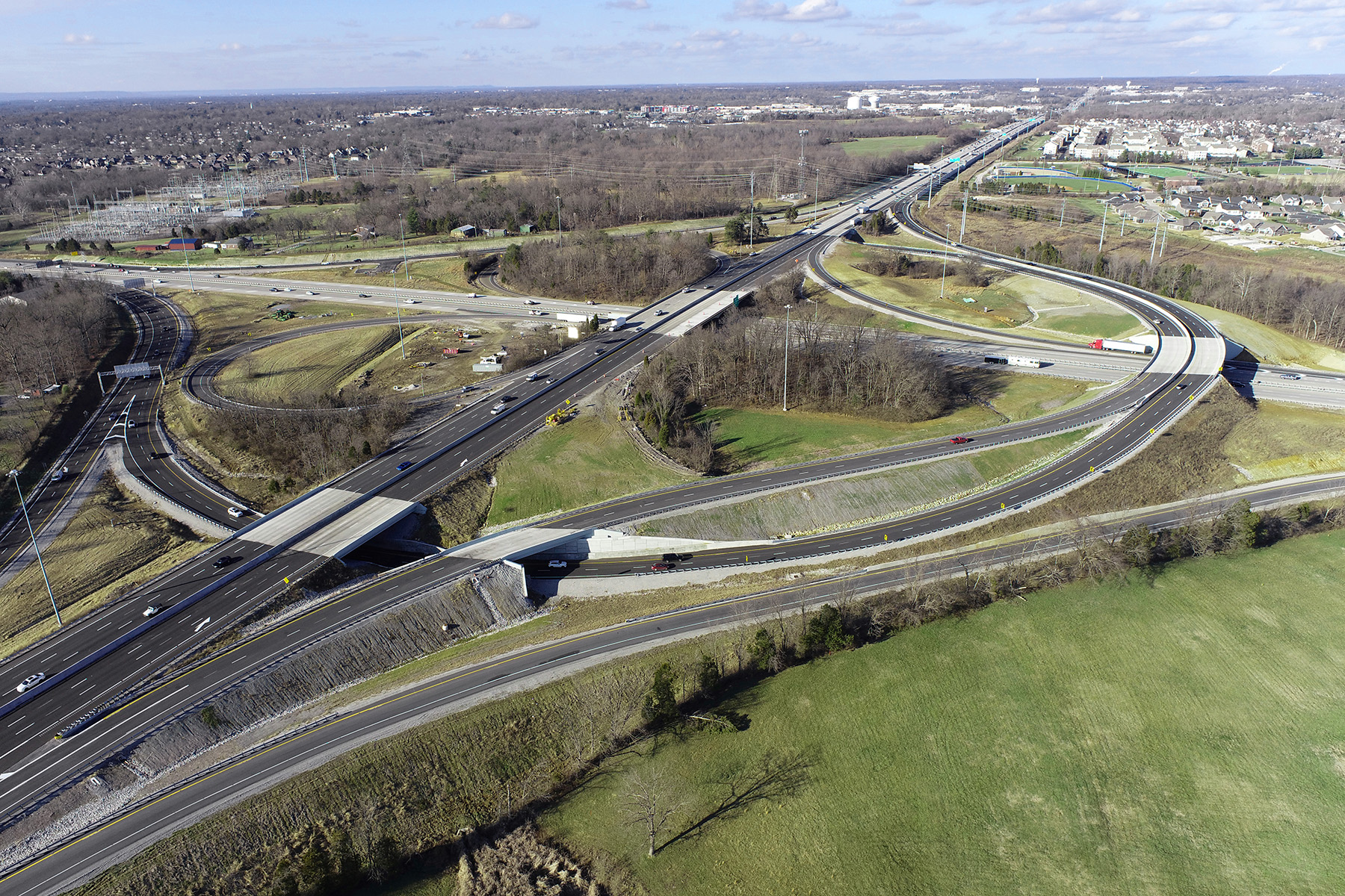 Photograph shows several highways and how they converge and separate through a major city. Some of the roads are straight and others are circular or semicircular. There are cars on the roads. 