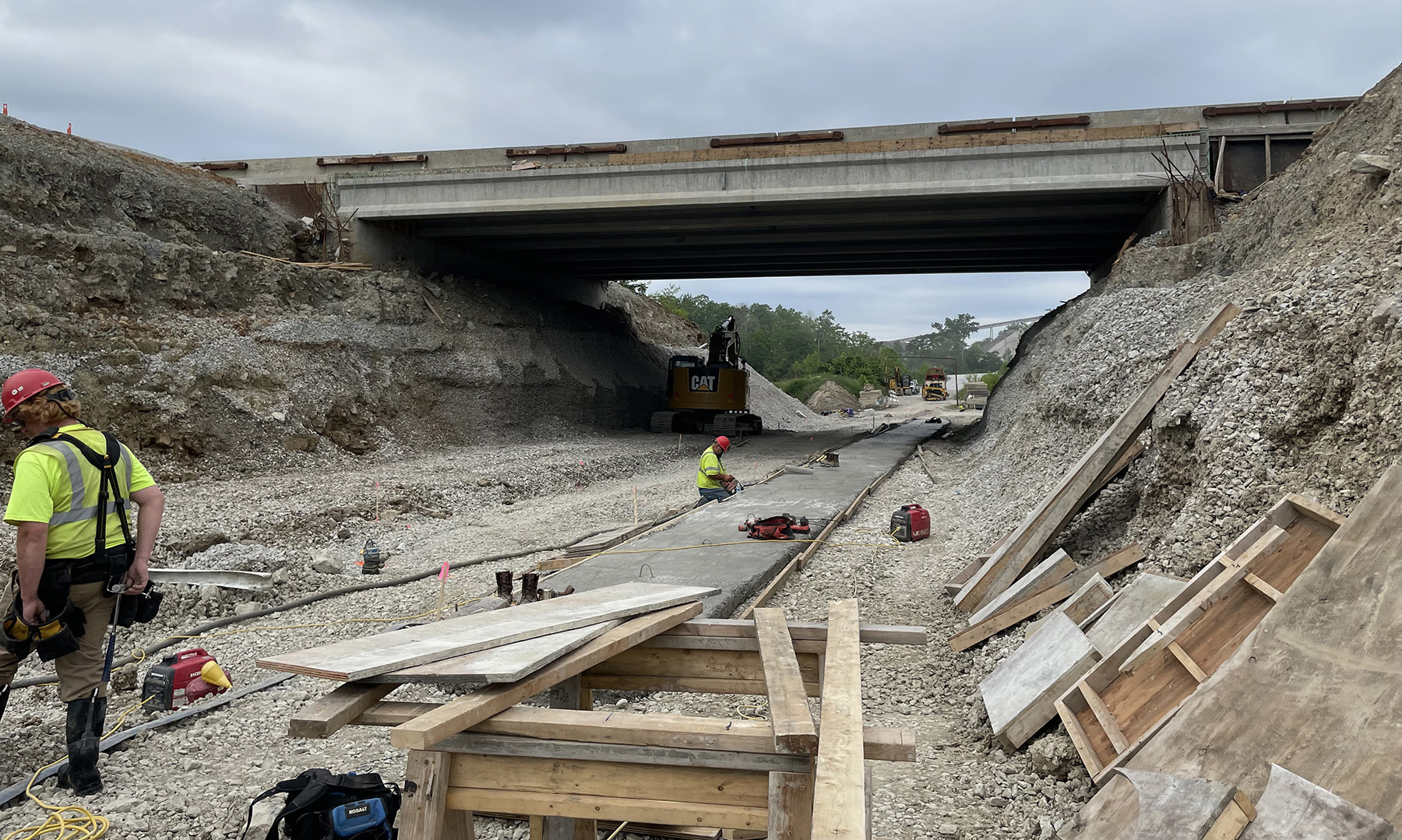 Men work on a culvert replacement underneath a bridge overpass. 