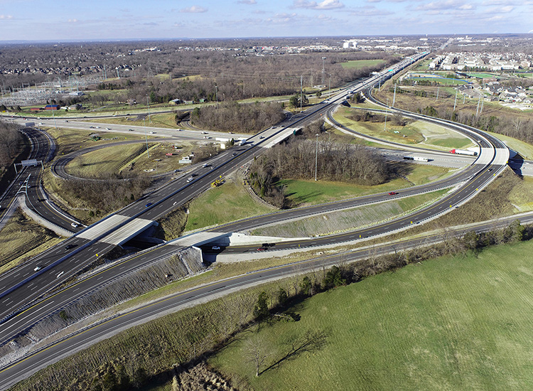 Photograph shows several highways and how they converge and separate through a major city. Some of the roads are straight and others are circular or semicircular. There are cars on the roads. 