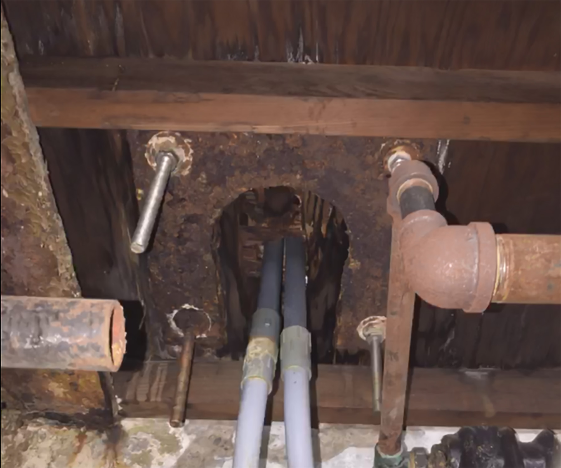 The photograph highlights the large bolts for a streetlamp seen from under the wooden beams of a basement ceiling. 