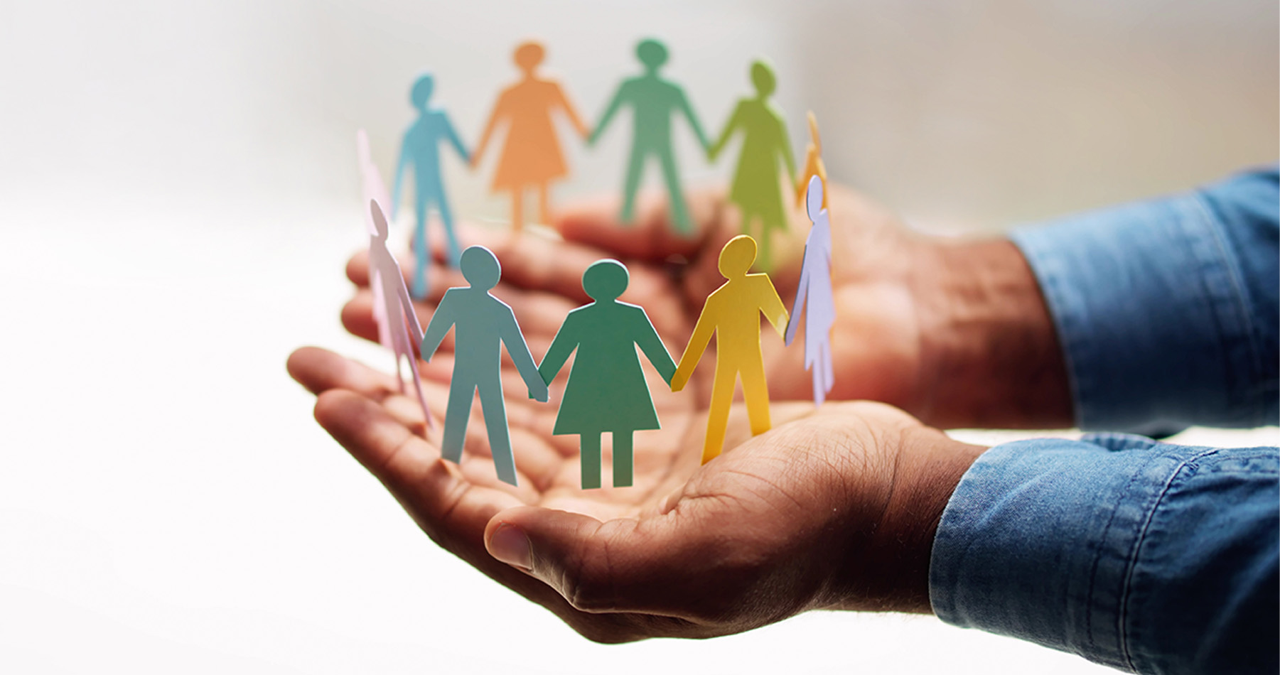 Man holds cut-out humanlike figures standing in a circle in his hand. 