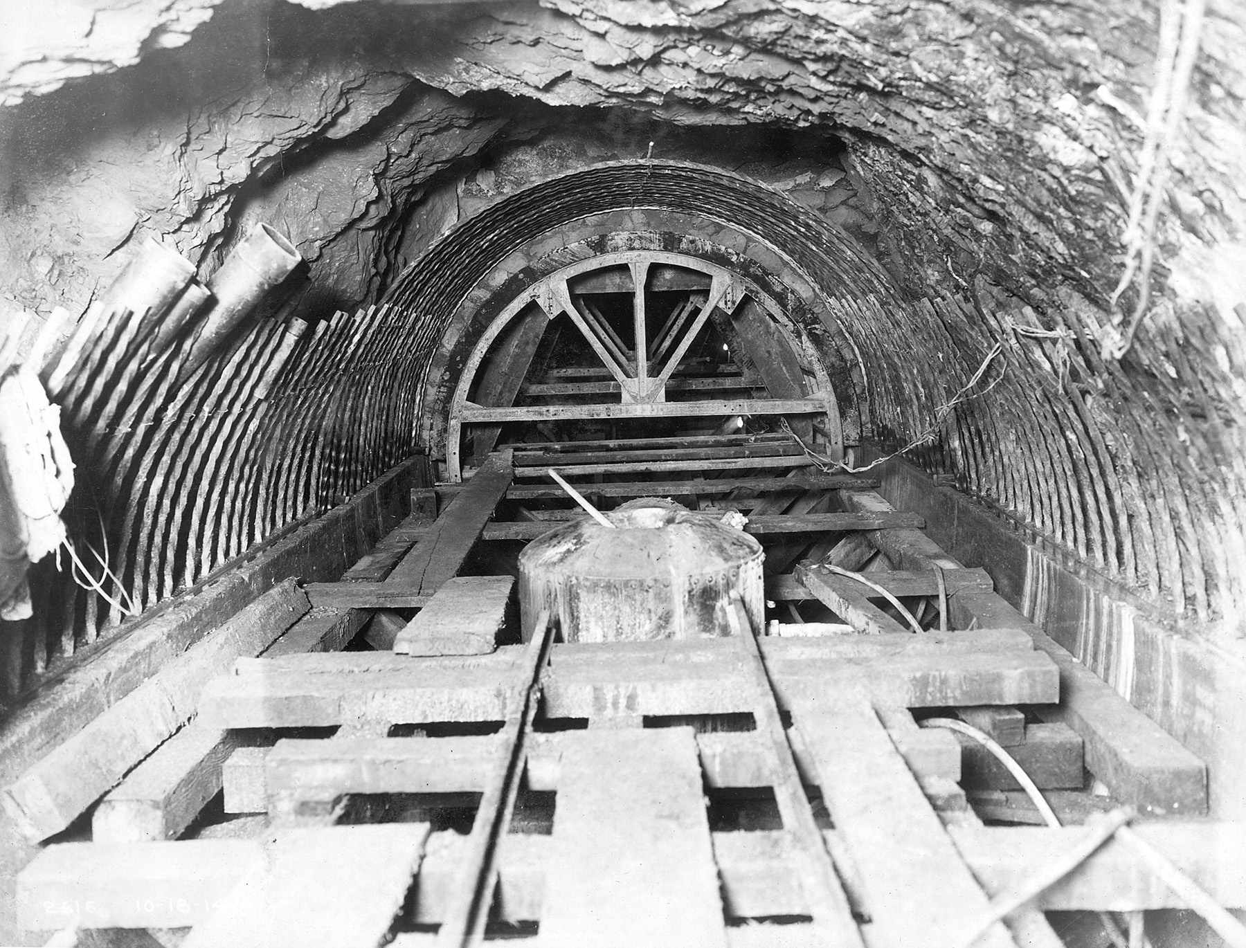 Image shows the interior of an outlet tunnel. Concrete and wood can be seen lining or inside the tunnel. There is wood formwork at the bottom of the tunnel. 