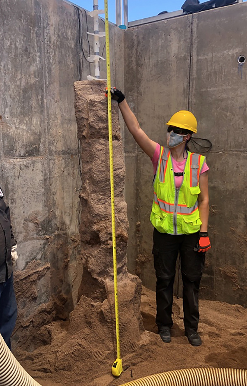 Photograph shows a person standing in a pit holding a measuring tape against a column of strengthened soil. The person wears protective safety equipment. 