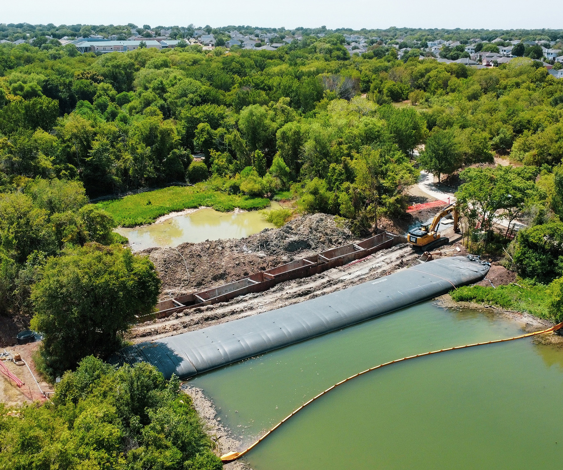An overhead view of the lake shows the dewatered side. There is an open trench with dirt piled up beside it and concrete rectangles sit in the trench.