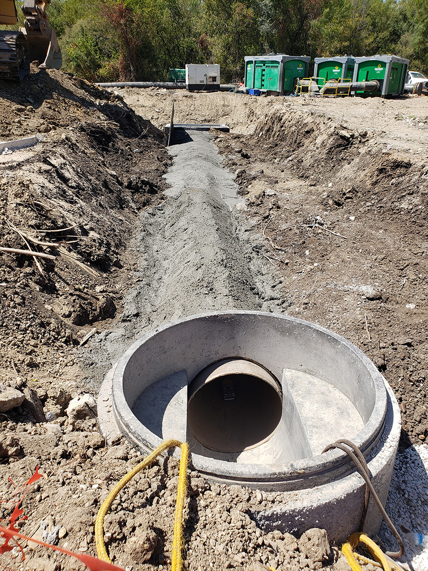 An up-close picture of the project’s buried piping is enclosed in concrete. There is a dirt trench in the background.
