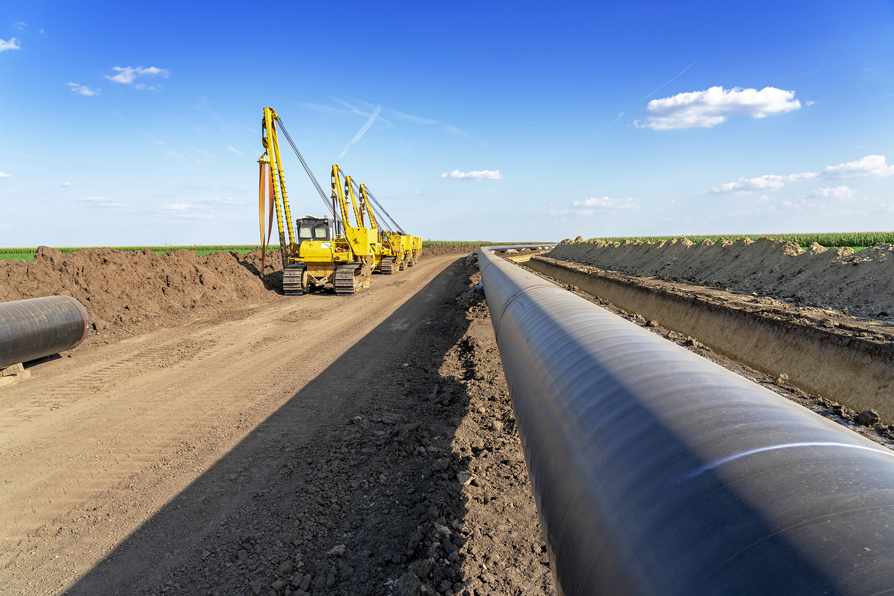 Picture shows a large-diameter pipe in the soil. To the left are three tractors used to dig out the earth. 